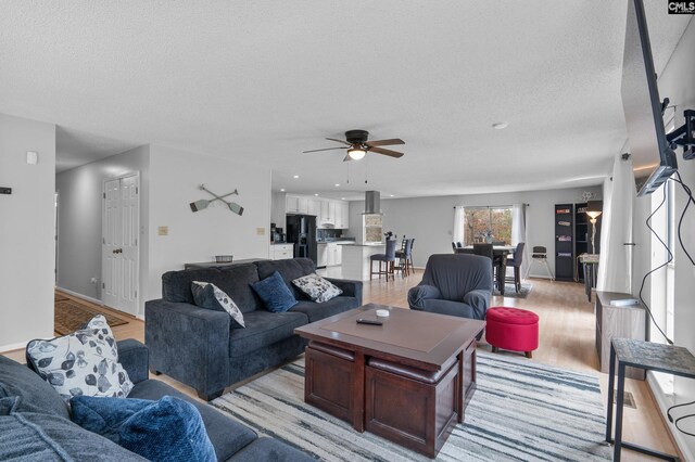 living room featuring a ceiling fan, a textured ceiling, and light wood finished floors