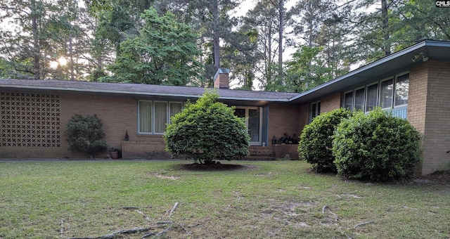 exterior space featuring brick siding, a yard, and a chimney