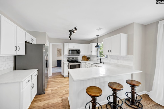 kitchen featuring appliances with stainless steel finishes, a sink, a peninsula, light wood-type flooring, and a kitchen bar