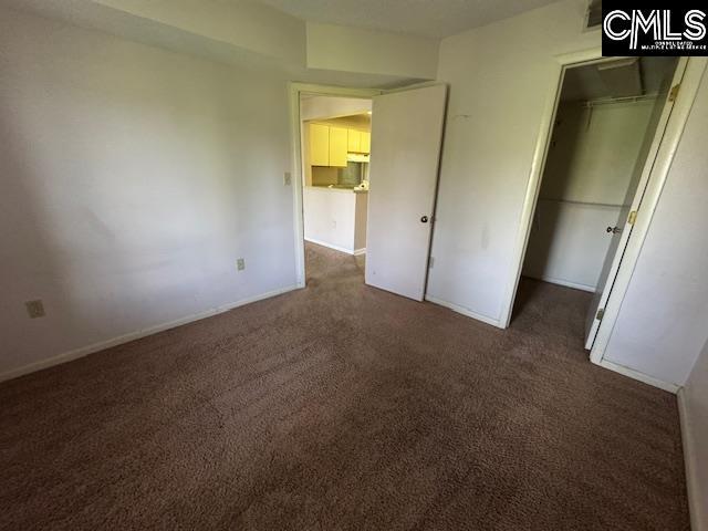 unfurnished bedroom with baseboards, dark carpet, and a closet
