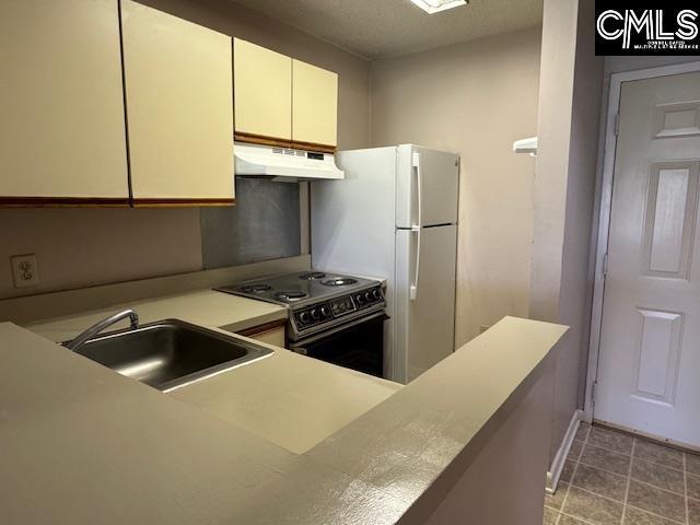 kitchen with a sink, light countertops, white cabinetry, under cabinet range hood, and range with electric stovetop