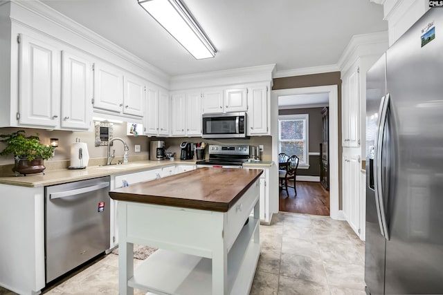 kitchen with crown molding, butcher block counters, white cabinets, a sink, and appliances with stainless steel finishes