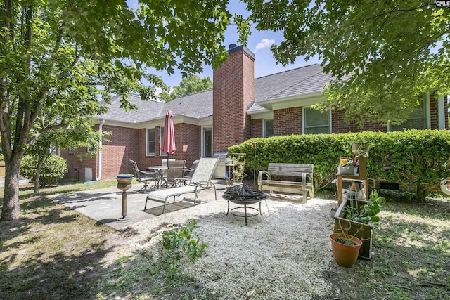 back of house with a chimney, brick siding, a shingled roof, a patio area, and an outdoor fire pit