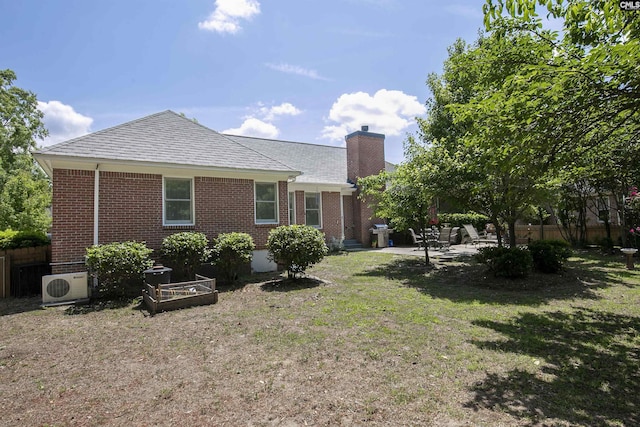 back of property with fence, a chimney, brick siding, a lawn, and ac unit