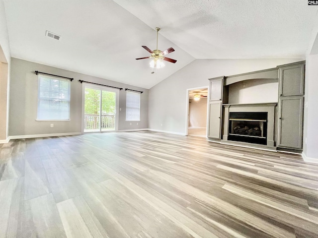 unfurnished living room featuring visible vents, a glass covered fireplace, lofted ceiling, ceiling fan, and light wood finished floors