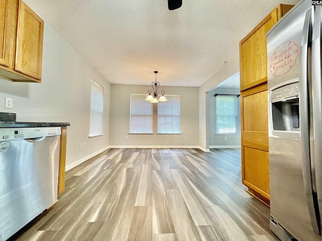 kitchen featuring baseboards, light wood-type flooring, a textured ceiling, a notable chandelier, and stainless steel appliances