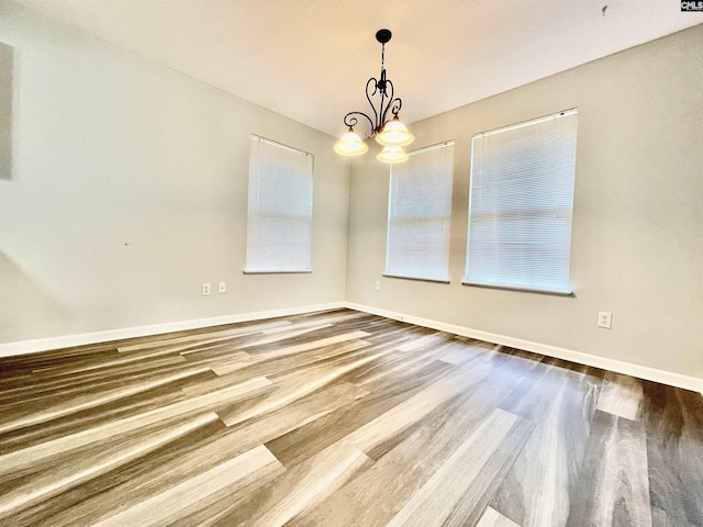 unfurnished dining area with baseboards, plenty of natural light, wood finished floors, and a notable chandelier