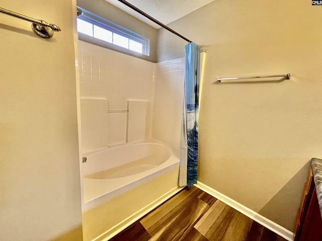 bathroom featuring baseboards, wood finished floors, and shower / bath combo