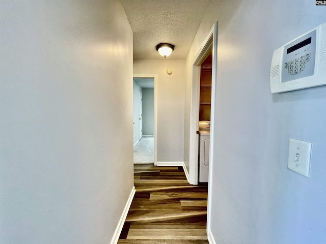 hall featuring baseboards, a textured ceiling, washer / clothes dryer, and wood finished floors