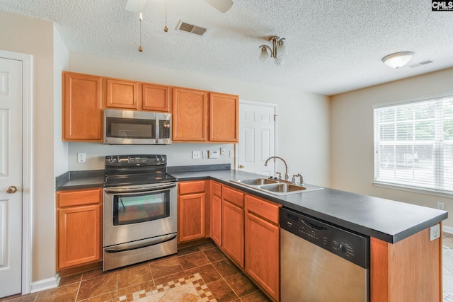 kitchen with visible vents, a peninsula, dark countertops, a sink, and stainless steel appliances