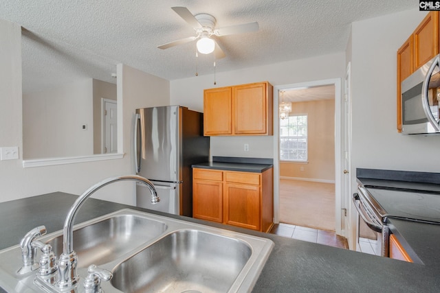 kitchen featuring dark countertops, light carpet, a sink, stainless steel appliances, and light tile patterned floors
