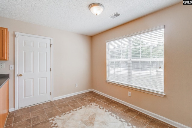 spare room with a textured ceiling, visible vents, plenty of natural light, and light tile patterned floors