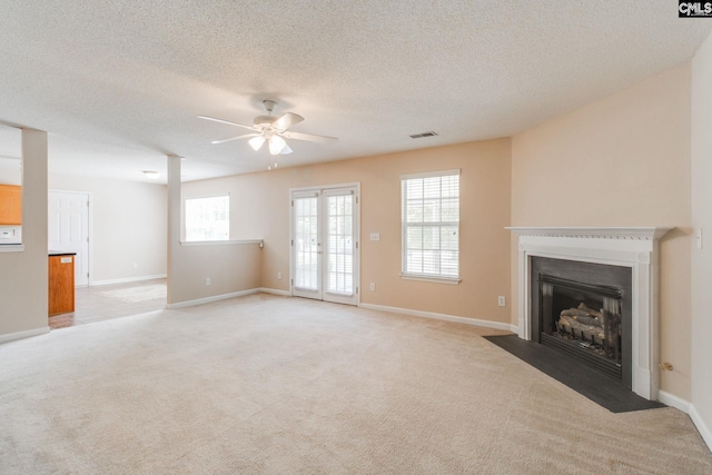 unfurnished living room with ceiling fan, visible vents, a fireplace with flush hearth, and light carpet