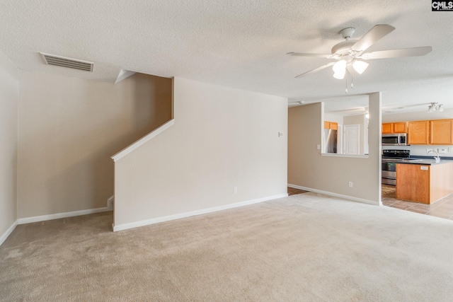 unfurnished living room featuring ceiling fan, visible vents, stairway, a sink, and light carpet