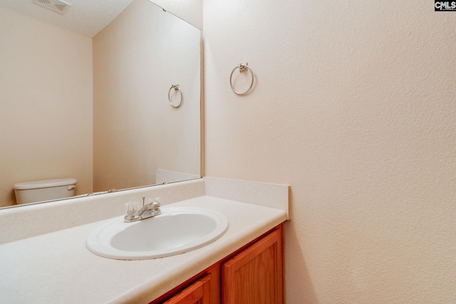 half bathroom featuring toilet, visible vents, and vanity