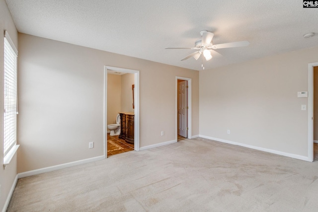 unfurnished bedroom featuring a ceiling fan, a textured ceiling, baseboards, light carpet, and ensuite bath
