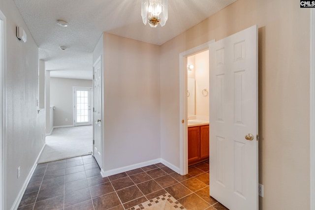 corridor featuring baseboards, a textured ceiling, and dark tile patterned floors