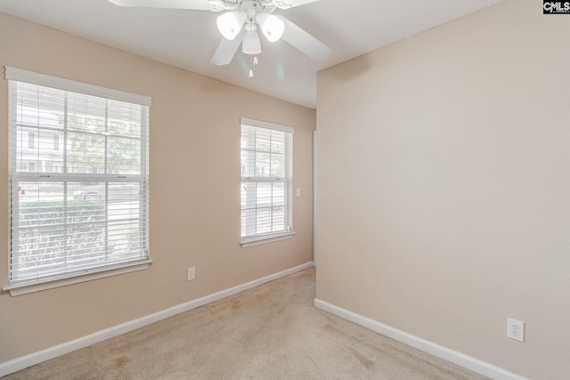 spare room featuring light colored carpet, a ceiling fan, and baseboards