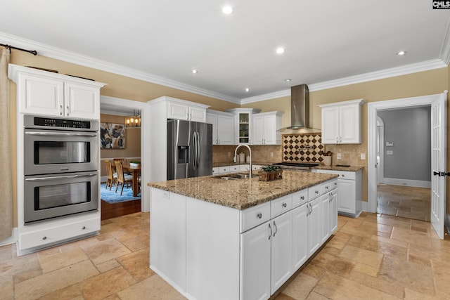 kitchen with crown molding, appliances with stainless steel finishes, a sink, wall chimney exhaust hood, and stone tile flooring