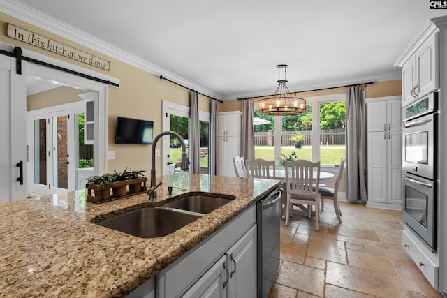 kitchen with a sink, appliances with stainless steel finishes, crown molding, and stone tile floors