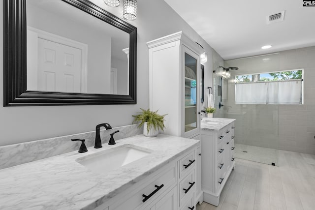 full bath featuring a walk in shower, visible vents, two vanities, and a sink