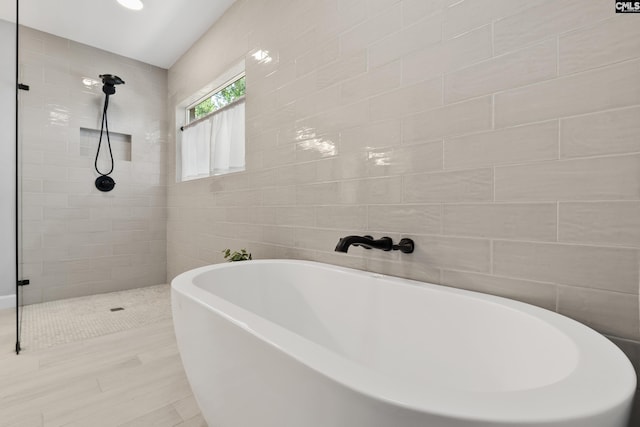 bathroom featuring tile walls, a tile shower, and a soaking tub
