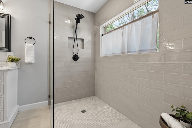 full bath with baseboards, a tile shower, wood finished floors, and vanity