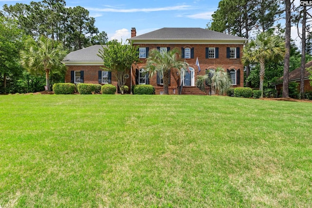 view of front of house featuring brick siding, a chimney, and a front lawn