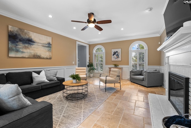 living room with a fireplace, ceiling fan, crown molding, and stone tile flooring