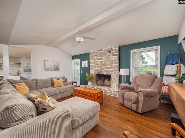 living room featuring vaulted ceiling with beams, a ceiling fan, a stone fireplace, and wood finished floors