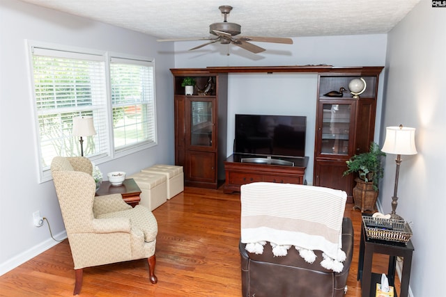 living area featuring baseboards, a ceiling fan, a textured ceiling, and wood finished floors