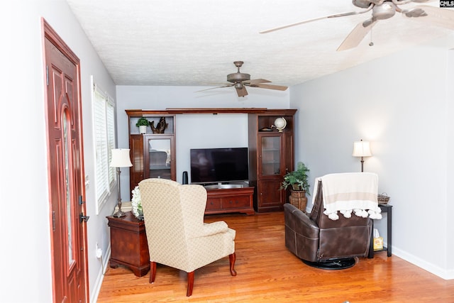living area featuring light wood-type flooring, a ceiling fan, a textured ceiling, and baseboards