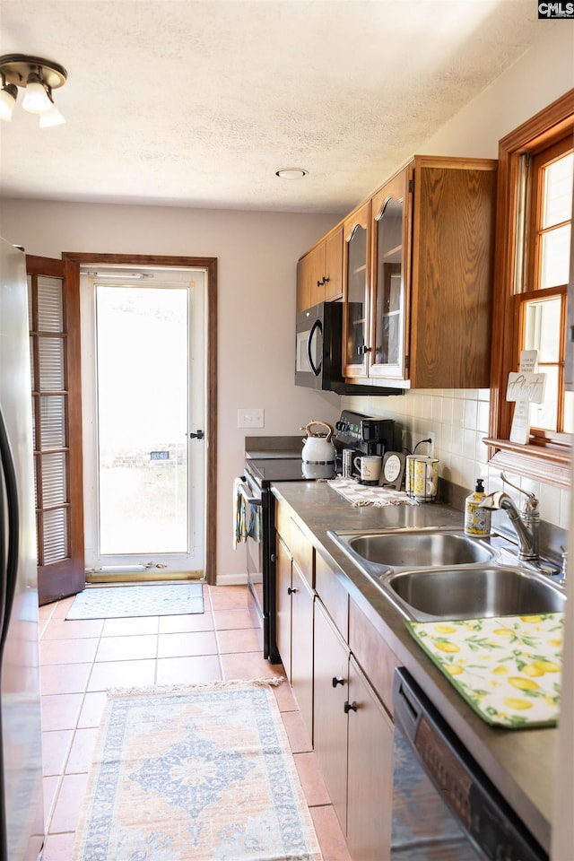 kitchen with glass insert cabinets, a textured ceiling, a sink, light tile patterned floors, and black appliances