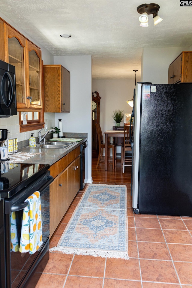 kitchen featuring brown cabinetry, a sink, light tile patterned floors, black appliances, and glass insert cabinets