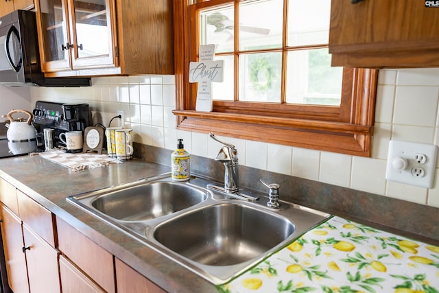 kitchen with a sink, glass insert cabinets, decorative backsplash, and dark countertops