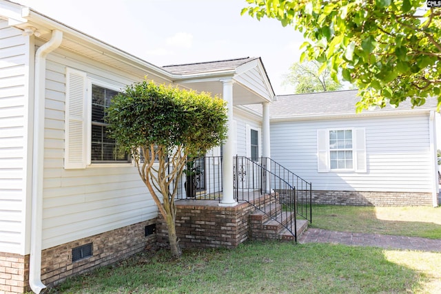 view of exterior entry with a lawn, crawl space, and roof with shingles