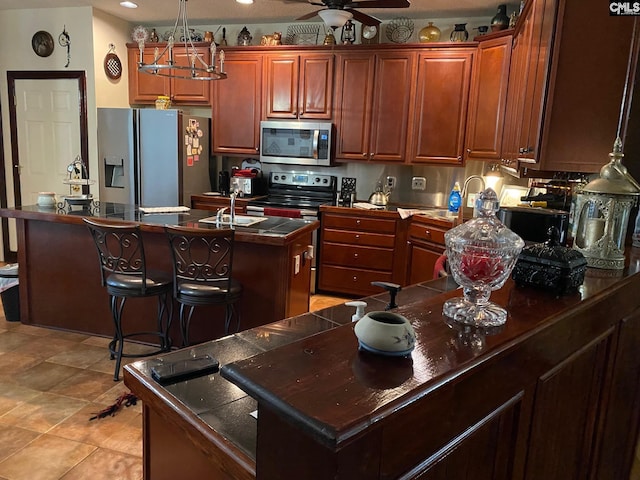 kitchen with ceiling fan, dark countertops, appliances with stainless steel finishes, a sink, and a kitchen island with sink