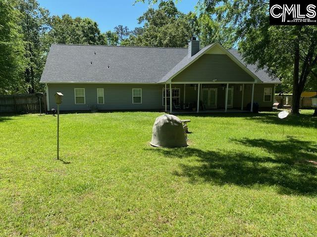 rear view of house featuring a yard, fence, and a chimney