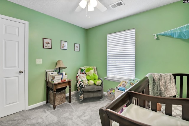 bedroom with a ceiling fan, visible vents, a crib, baseboards, and carpet flooring