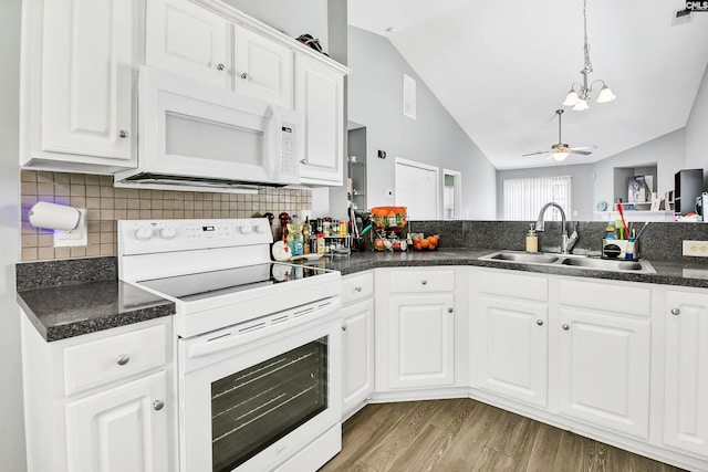 kitchen featuring dark countertops, a sink, white appliances, wood finished floors, and vaulted ceiling