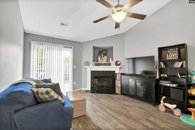 living room featuring a ceiling fan, a fireplace with flush hearth, wood finished floors, vaulted ceiling, and visible vents