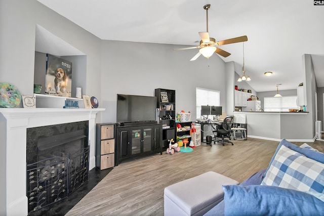 living room featuring ceiling fan, a fireplace with flush hearth, wood finished floors, baseboards, and lofted ceiling