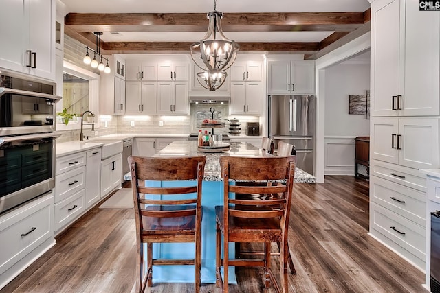 kitchen with beamed ceiling, appliances with stainless steel finishes, decorative backsplash, and a sink