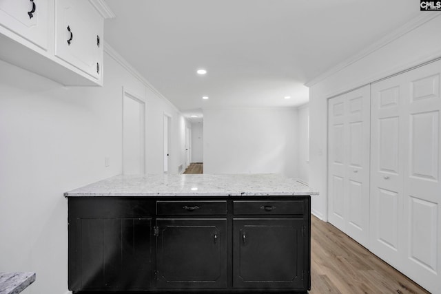 kitchen featuring dark cabinetry, crown molding, light wood-style floors, and a peninsula