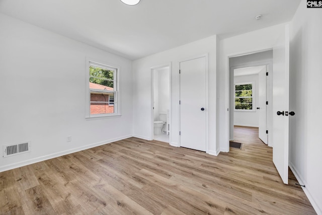 unfurnished bedroom with visible vents, light wood-style flooring, ensuite bath, and baseboards