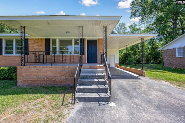 view of front facade featuring a front lawn, brick siding, an attached carport, covered porch, and driveway