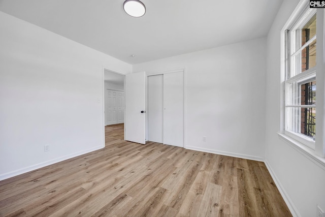 unfurnished bedroom with baseboards, multiple windows, wood finished floors, and a closet