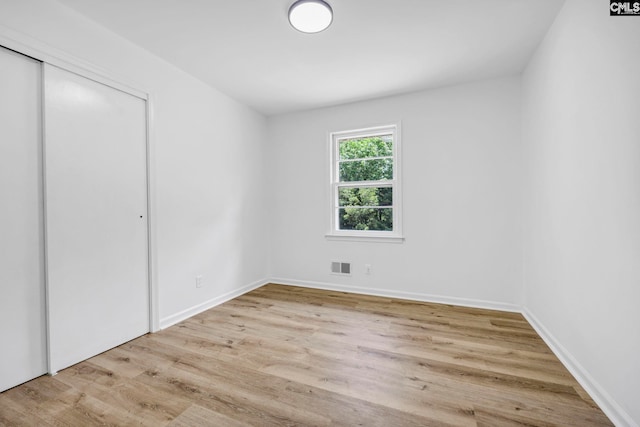 unfurnished bedroom featuring baseboards, visible vents, wood finished floors, and a closet