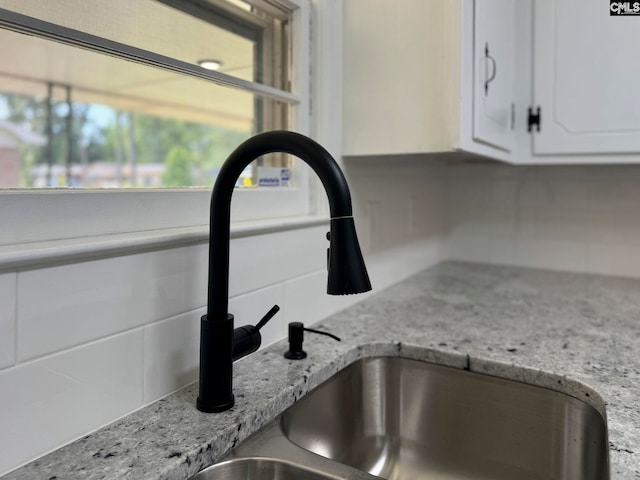 interior details with a sink, light stone counters, decorative backsplash, and white cabinetry