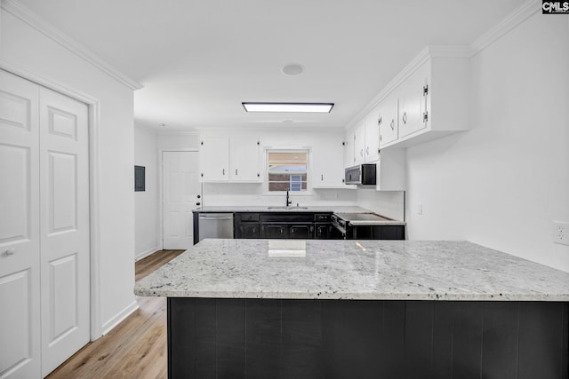 kitchen with white cabinets, appliances with stainless steel finishes, a sink, light wood-type flooring, and ornamental molding